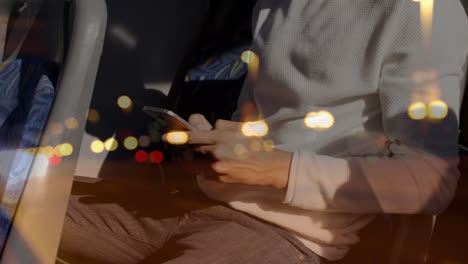 spots of bokeh lights against mid section of man using smartphone in a bus