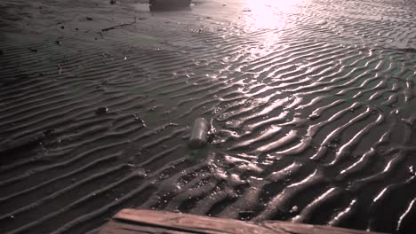 Slowly-rotating-view-of-a-plastic-bottle-stuck-in-the-sand-with-ripples-left-behind-from-the-rivers-current