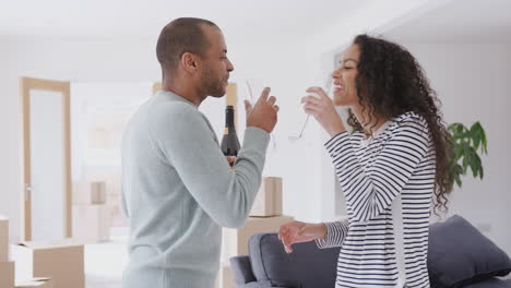 loving couple surrounded by boxes celebrating moving into new home with champagne