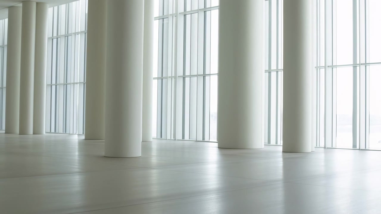 Slow lateral movement follows a bright minimalist hall with repeating round columns, expansive glass windows, pale reflective flooring, and evenly diffused natural light.