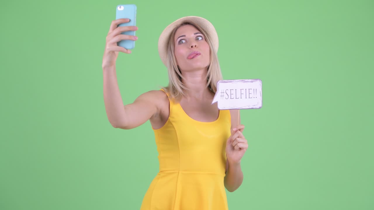 fotografía de estudio de una joven turista tomando una selfie con un teléfono móvil contra un fondo verde
