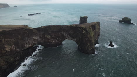 Wide-aerial-parallax-around-Dyrholaey-Arch,-or-Arch-With-the-Hole,-in-Iceland