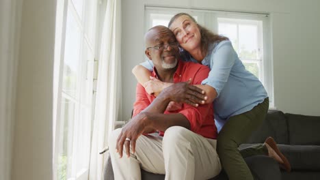 Happy-senior-diverse-couple-wearing-shirts-and-embracing-in-living-room