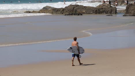 a surfer walks towards the ocean waves