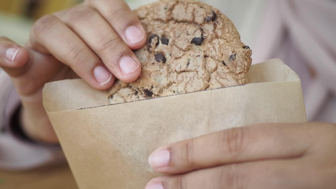 persona comiendo una galleta de chispas de chocolate de una bolsa de papel