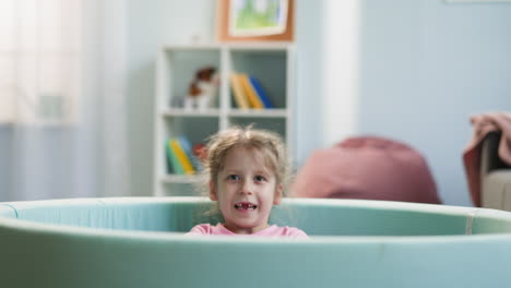 toothless preschooler throws balls up lying in dry pool