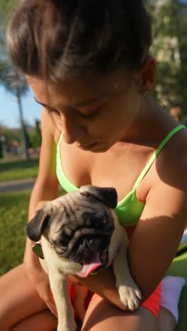 mujer en ropa deportiva sosteniendo un perro pug en un parque
