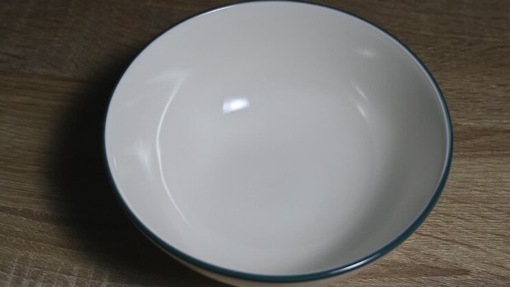 Ciotola bianca di ceramica sul tavolo, in primo piano, prima di essere riempita con cereali o granola durante la colazione