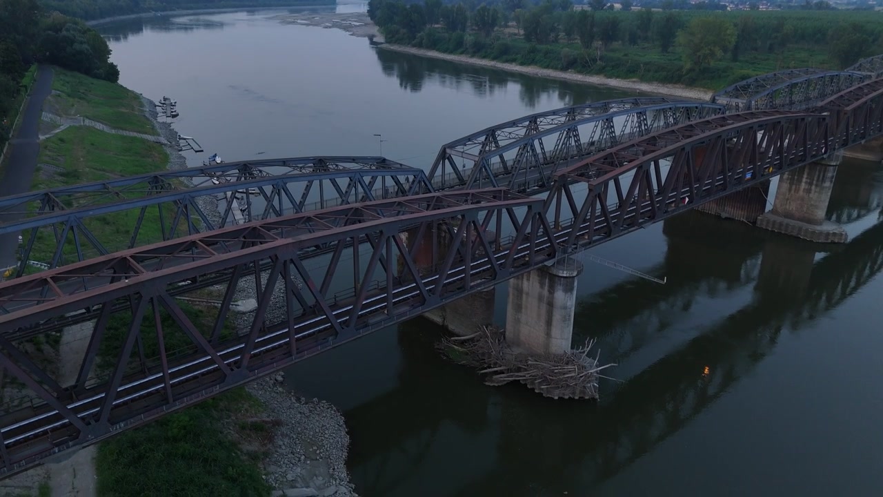 Po River beneath Ponte di Ferro railway and road bridges, Cremona, Lombardy, Italy, reaches record low levels during the June 2026 heatwave, exposing vast sandbanks. Slow aerial drone orbit.