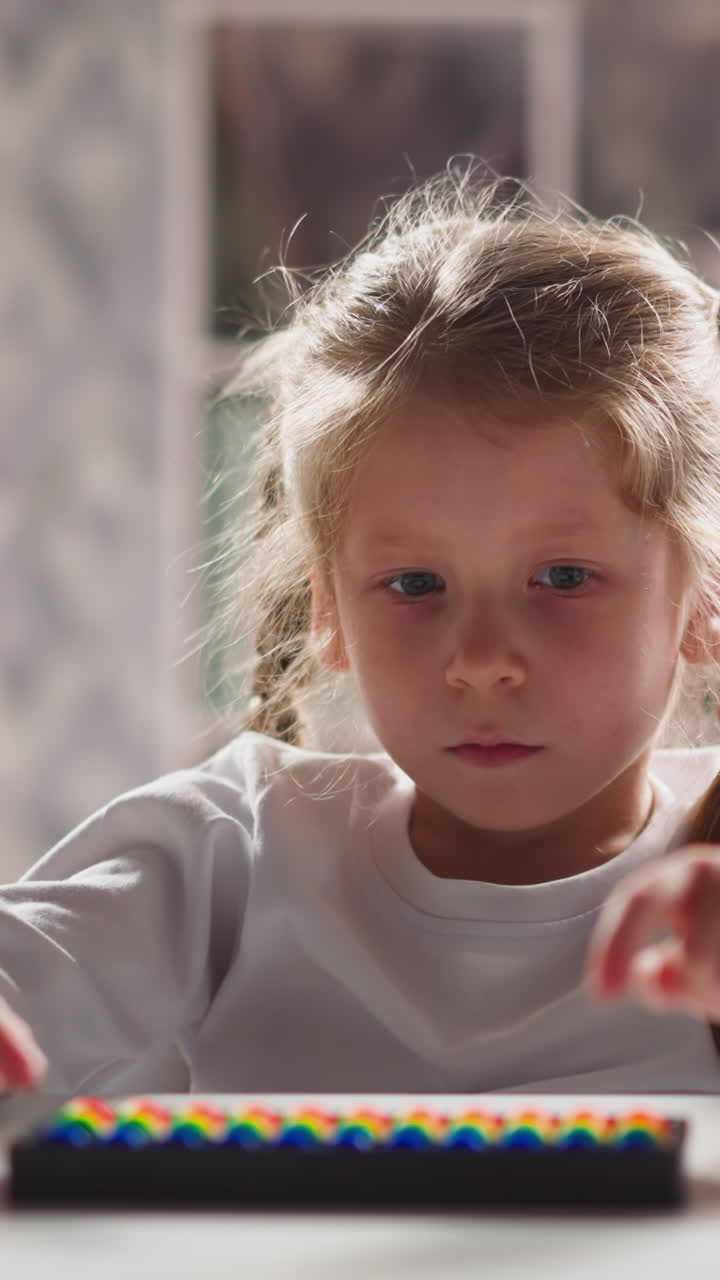 Upset little girl student plays with toy abacus learning mental arithmetics at table in kindergarten classroom close view slow motion