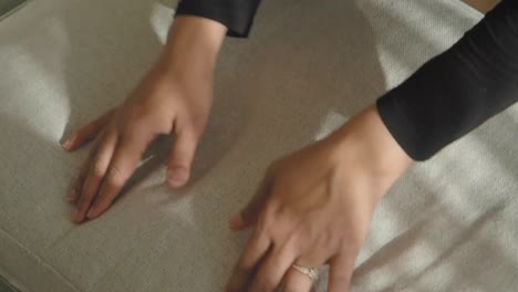 a hand patting a couch cushion with sunlight creating striped shadows