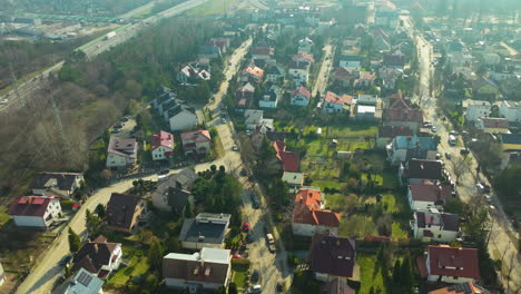 An-aerial-view-of-a-suburban-neighborhood-with-rows-of-detached-houses,-gardens,-and-tree-lined-streets,-near-a-highway-that-borders-a-dense-forest-area