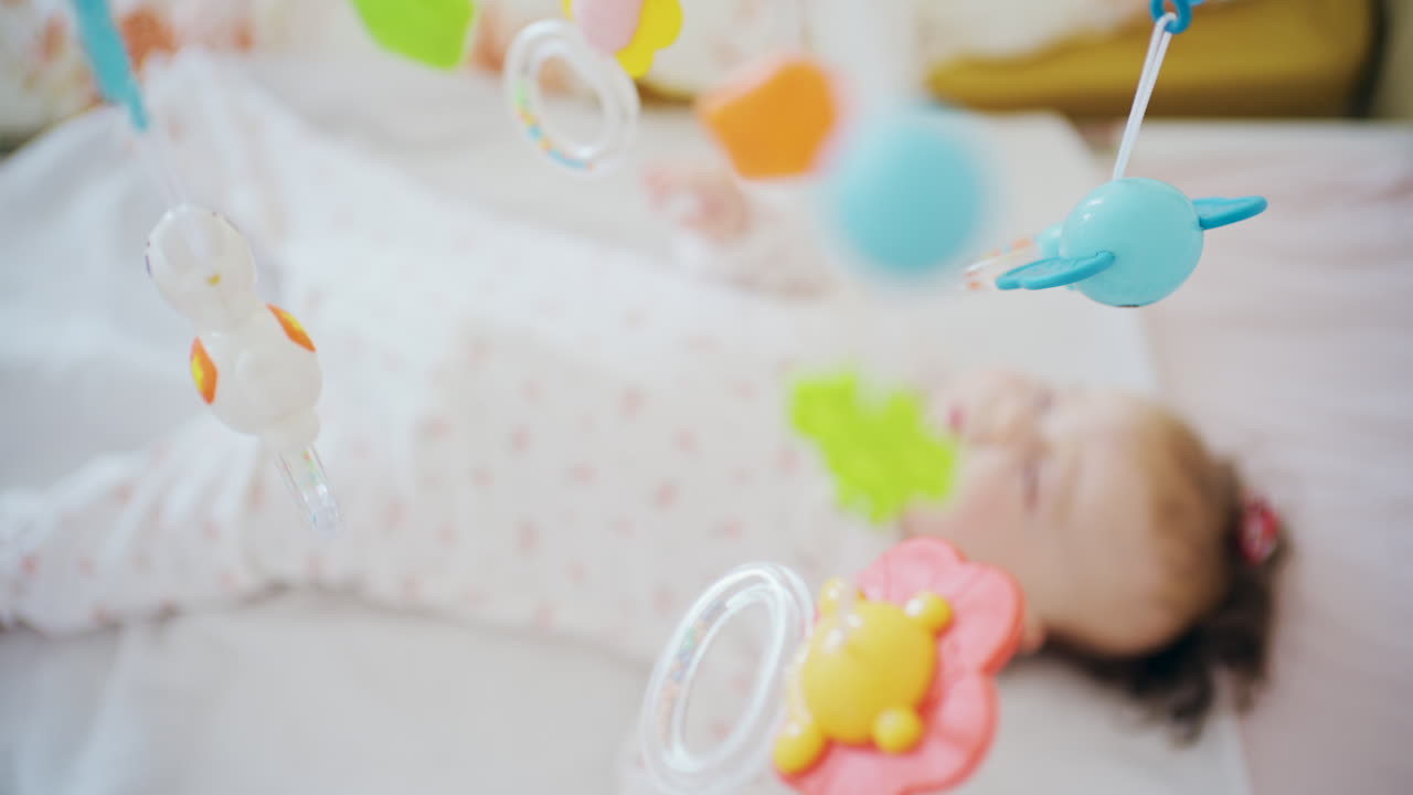 Infant lying in crib looking at colorful mobile toys hanging above
