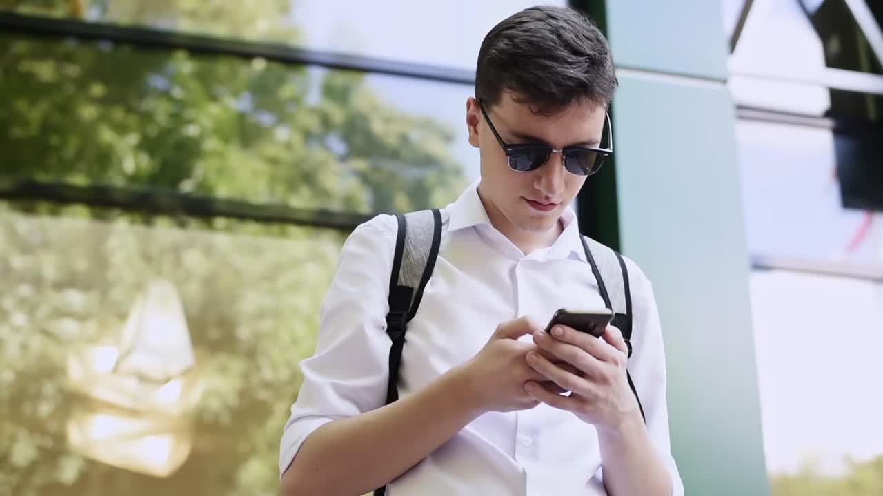 Caucasian man in white shirt and sunglasses writing messages on the phone. Sunny day
