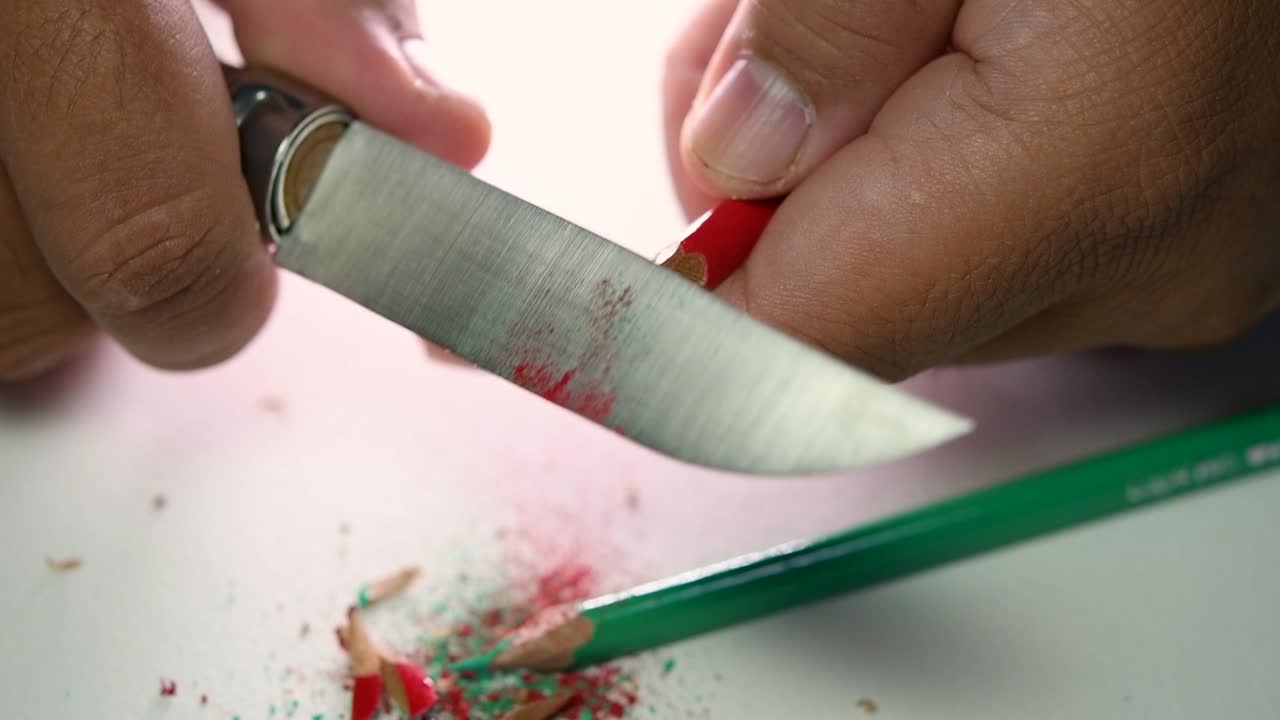 Beelden van handen die langzaam een potlood en enkele kleurpotloden slijpen met een scherp mes.
