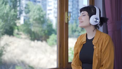 young woman looking out the window and listening to music with headphones.