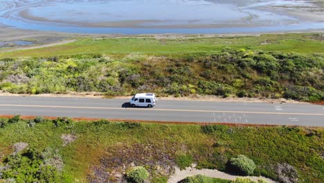 Video-De-Un-Dron-De-Una-Camioneta-Blanca-Viajando-Por-Una-Carretera-Con-Una-Solución-Salina-De-Fondo,-El-Dron-Sigue-A-La-Camioneta-Antes-De-Ascender-Para-Revelar-La-Inmensidad-De-La-Solución-Salina,-En-Bodega-Bay,-California