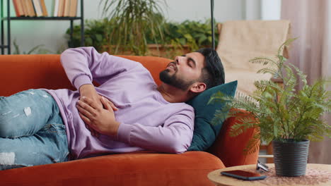 Indian-man-lying-on-sofa-feeling-sudden-strong-abdominal-stomach-ache,-gastritis-problem,-diarrhea