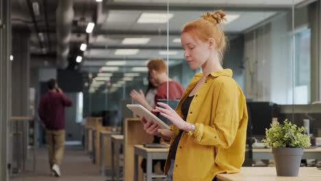 young redhead businesswoman in yellow jacket using tablet in office