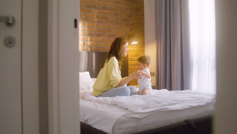 woman helping her baby get up and hugging him while sitting on the bed at home