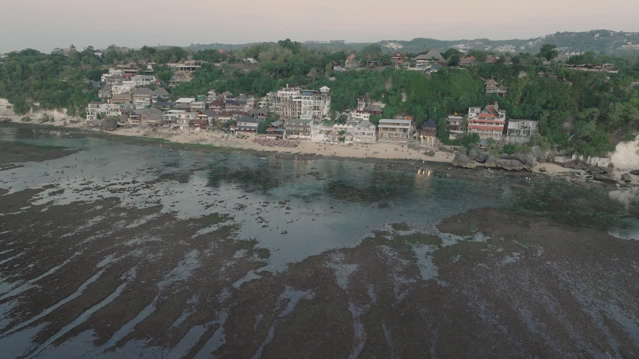 en la lejanía, una fotografía de aviones no tripulados de los edificios de la playa de bingin al atardecer y la marea baja en uluwatu bali, indonesia