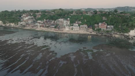 Far-away-Panning-Drone-shot-of-Bingin-Beach-buildings-at-sunset-and-low-tide-in-Uluwatu-Bali-Indonesia