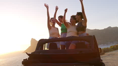 amigas de pie a través del techo del sol del coche bailando en un viaje por carretera