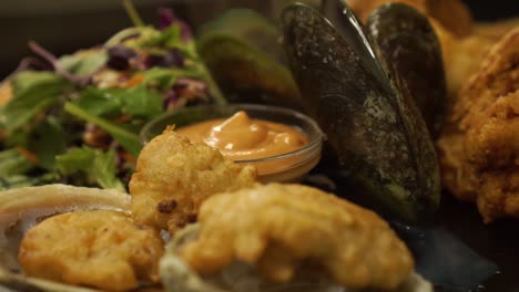 chef finishing dish new zealand greenshell mussells on plate with green salad, oysters and gravy - close up