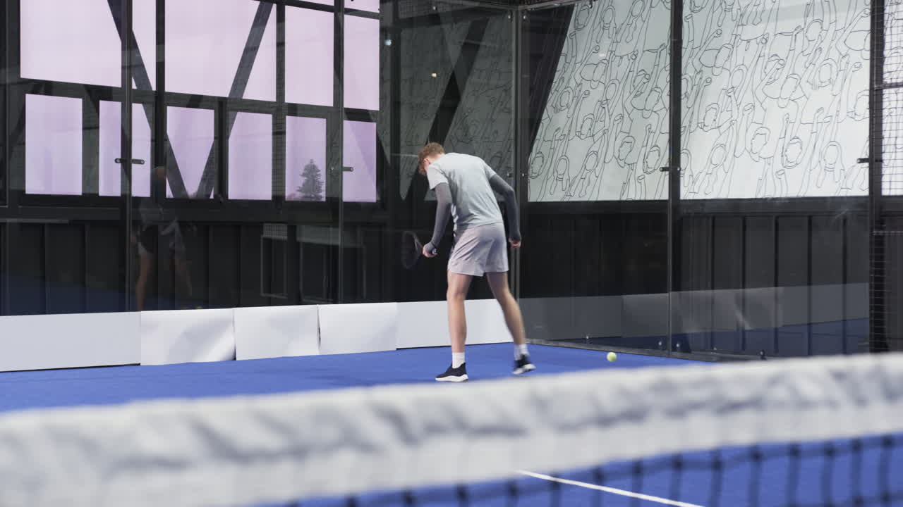 Young man playing padel tennis indoors, focusing on returning ball, at indoor court