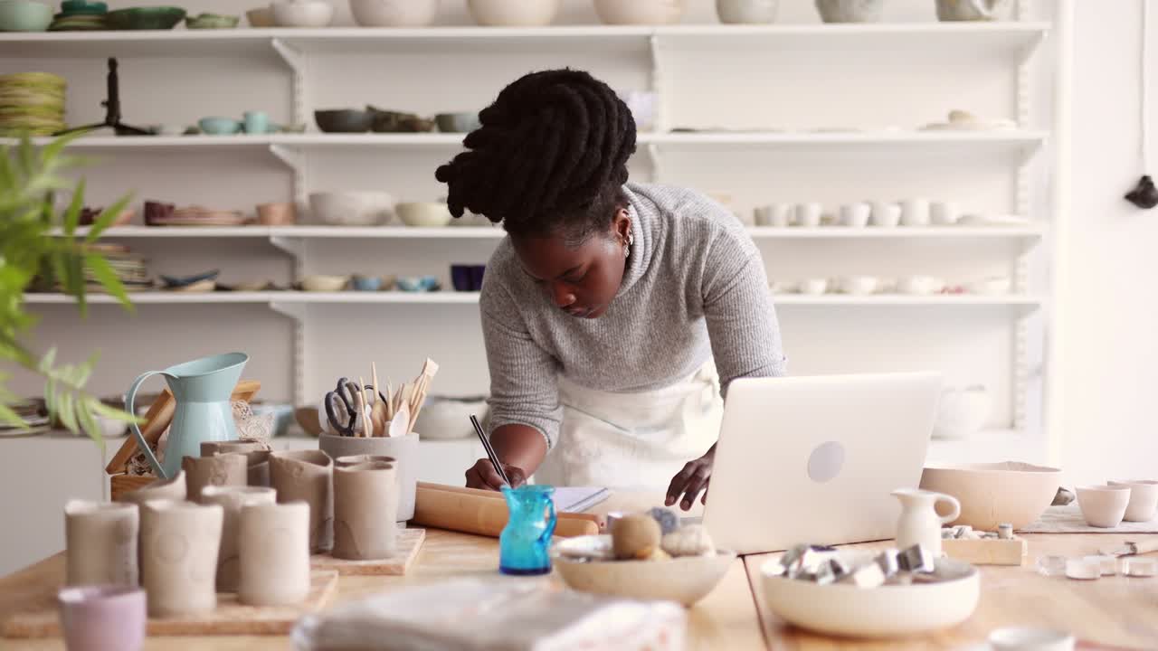 Young female pottery artist using laptop in her workshop