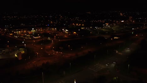 Nighttime-traffic-headlights-driving-dark-British-town-highway-intersection-aerial-view