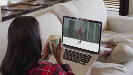 Compuesto-De-Una-Mujer-Sentada-En-Casa-Sosteniendo-Un-Café-Viendo-Un-Evento-De-Atletismo-En-Una-Computadora-Portátil