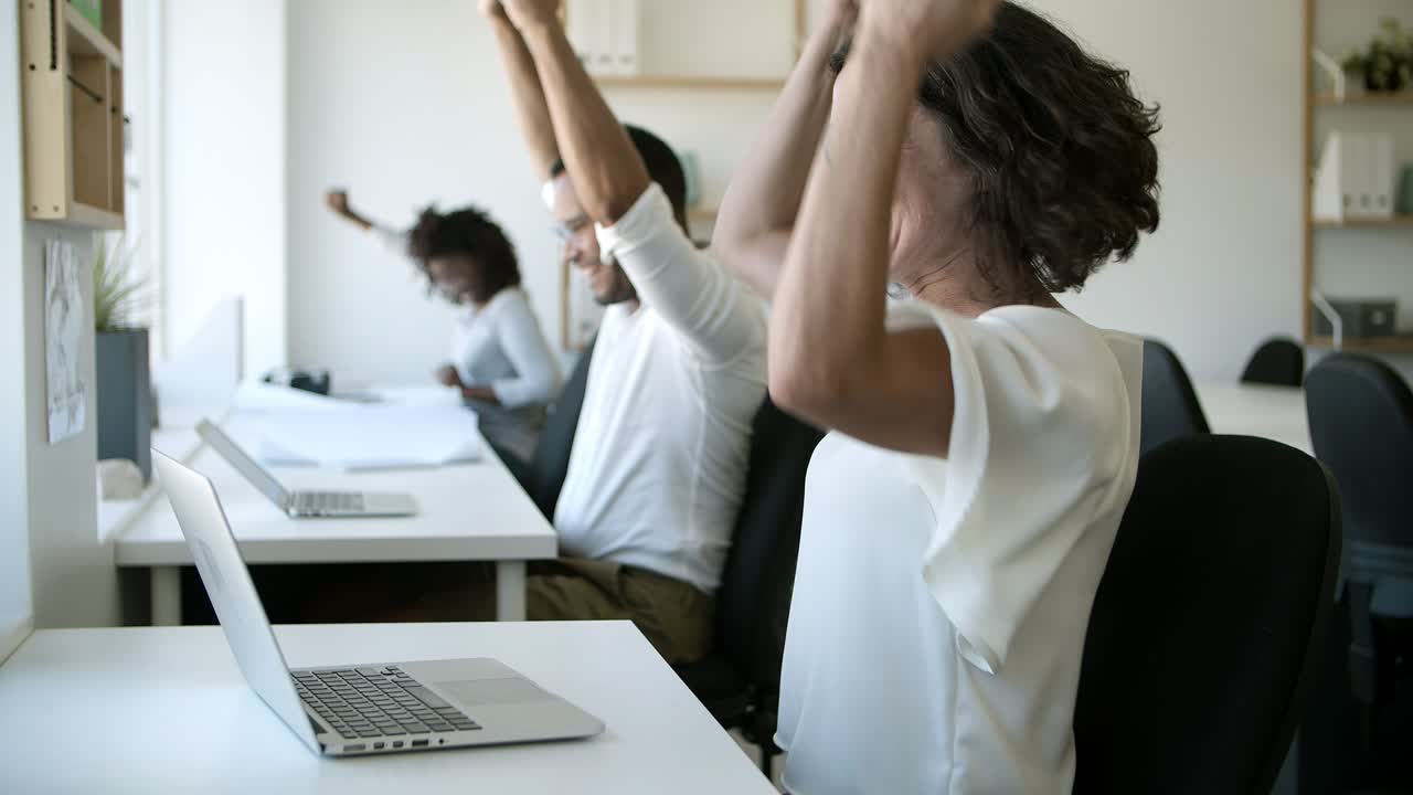 Curly woman looking at laptop then giving high five to colleagues