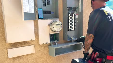 instalador que usa una aspiradora para limpiar el polvo y la suciedad de la caja de control del panel solar en el costado de la casa
