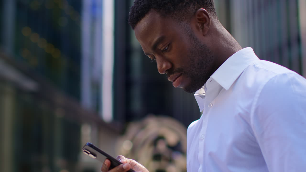 Young Businessman In Shirt Sleeves Looking At Mobile Phone Standing Outside Offices In The Financial District Of The City Of London UK 1