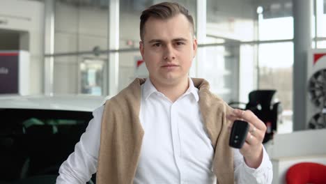 elegant stylish man showing keys of his new car in dealership