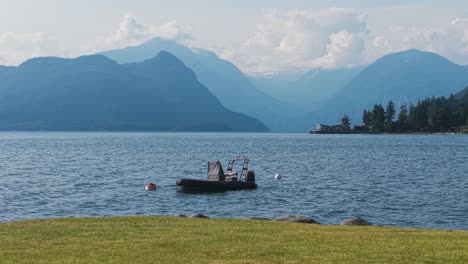 a calm seaside in lions bay surrounded by stunning mountains features a small fishing boat. the clear water reflects the serene landscape, perfect for outdoor leisure and nature appreciation