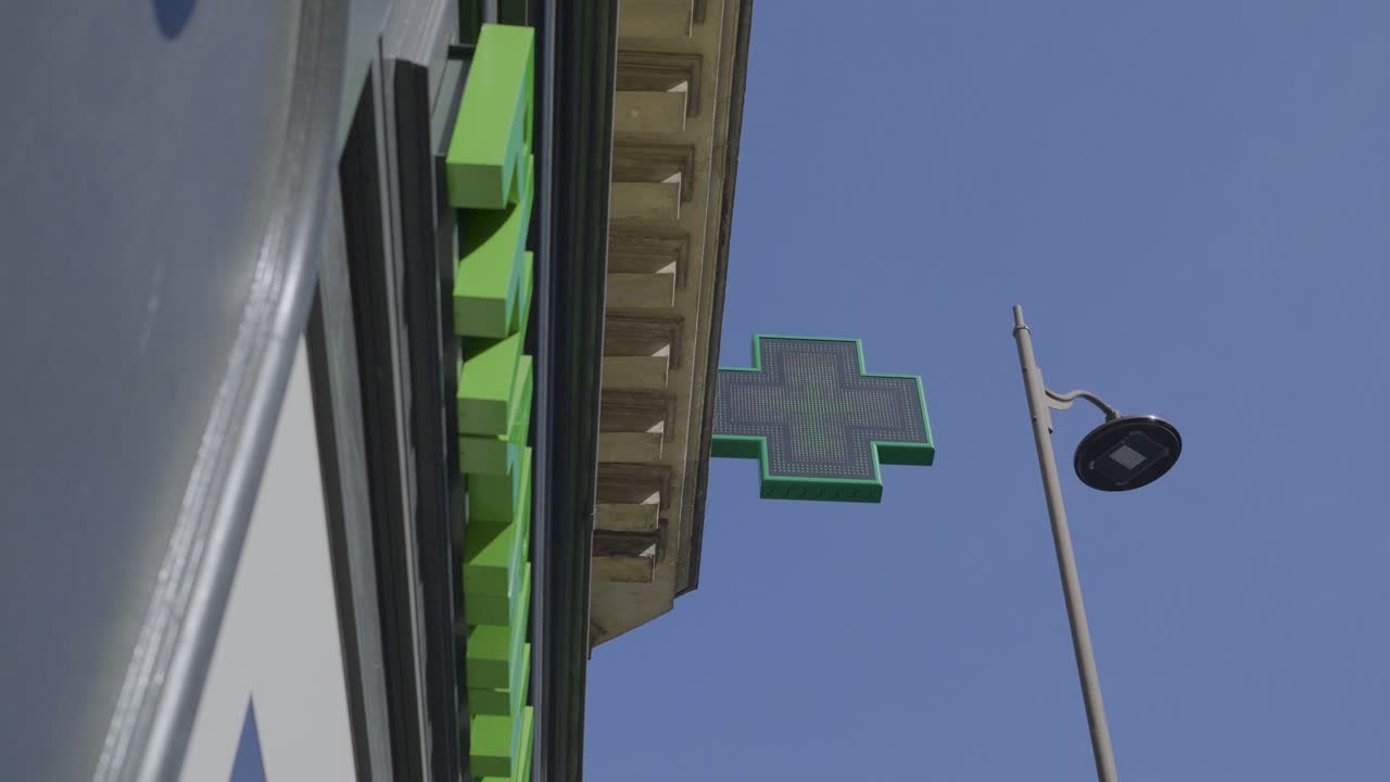 Green pharmacy cross sign against a bright sky in Paris, France, capturing the vibrant atmosphere