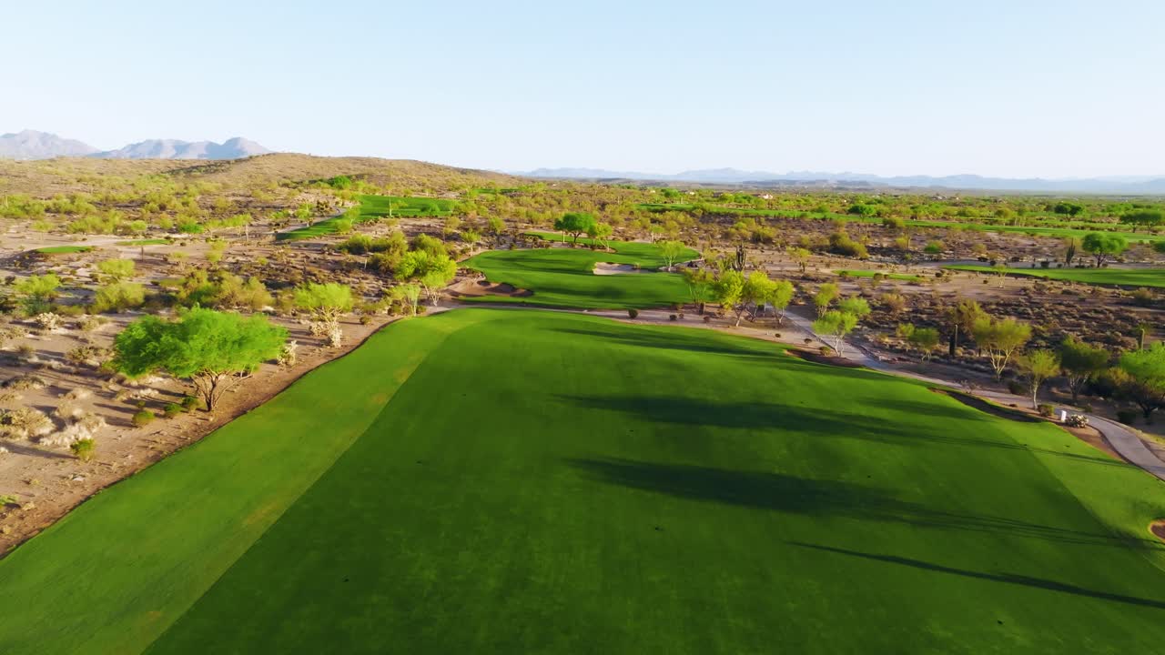 Aerial push-in shot over a lush desert golf fairway surrounded by dry terrain and mountain views