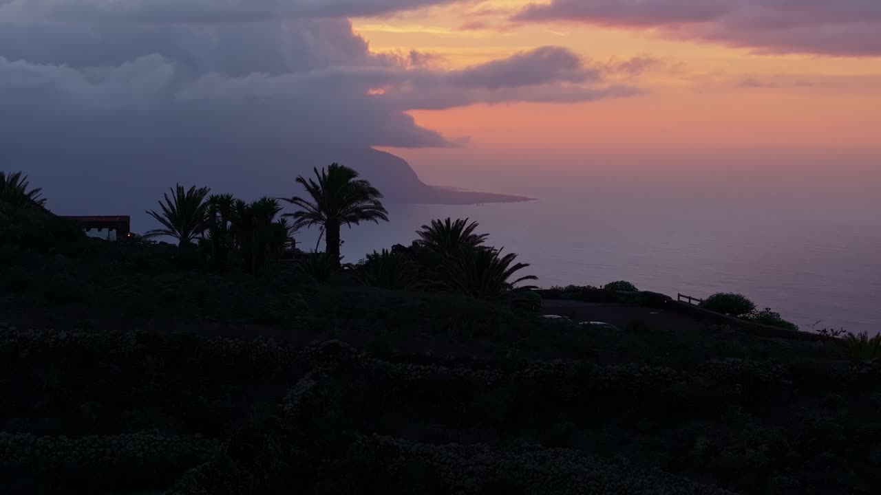 Sunset over the Canary Islands with dark silhouettes of palm trees and coastline