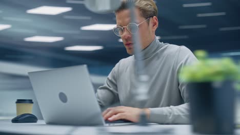 Modern Office: Handsome Businessman Sitting at His Desk Working on a Laptop Computer. Man working with Big Data e-Commerce Analysis. Energetic 360 Degree Fast Tracking Shot. Camera Moving Around