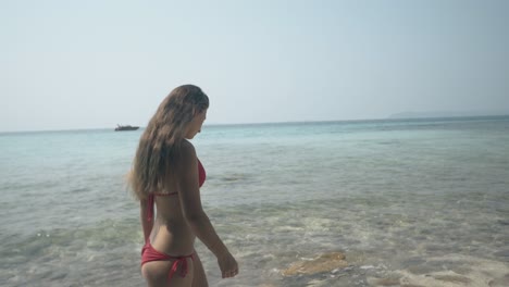 girl in red bikini walks along tropical beach against ocean