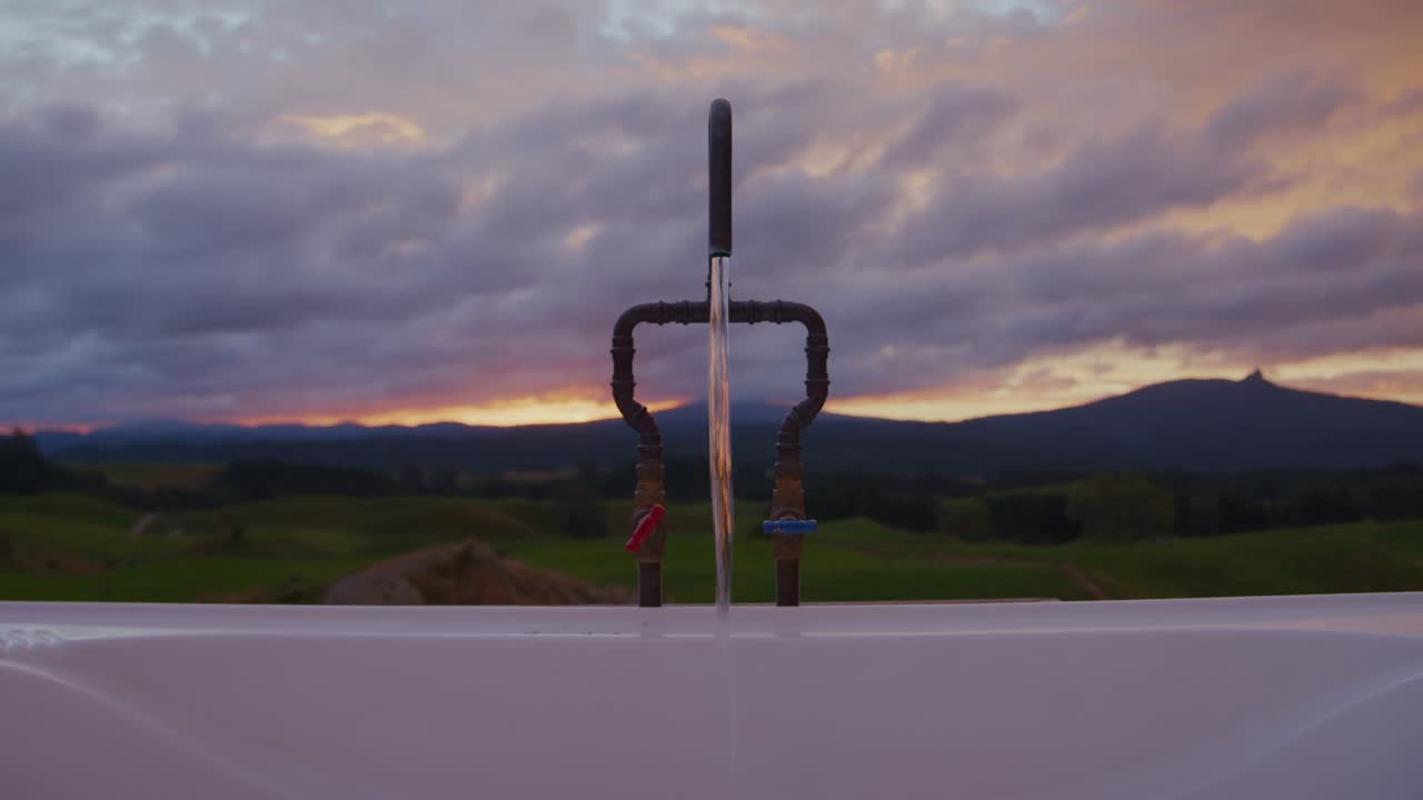 Bagno nelle montagne della Nuova Zelanda. Primo piano statico con messa a fuoco che passa dal primo piano allo sfondo. Sfondo al tramonto arancione sopra verdi campi aperti.
