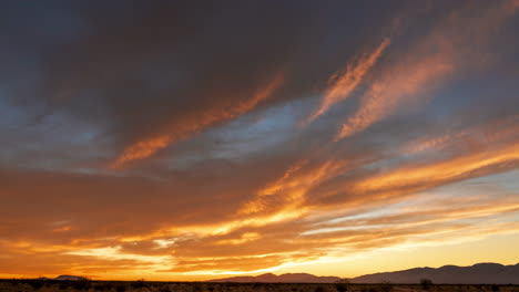 el cielo brilla de oro a rojo brillante sobre el desierto de mojave mientras el sol se pone más allá de las montañas occidentales - lapso de tiempo de gran angular