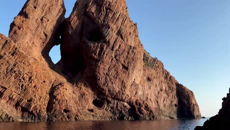 hole in red rock of scandola peninsula nature reserve in summer season as seen from moving boat, corsica island in france