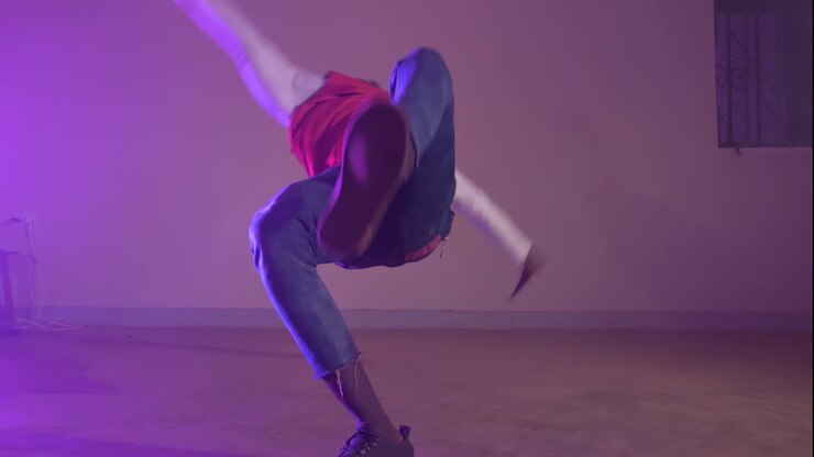 Slow motion shot of African youth in a red shirt twisting his body on his hands while break dancing in colorful lights