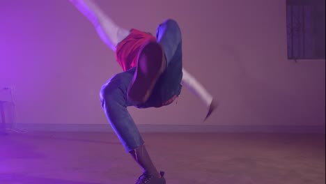 slow motion shot of african youth in a red shirt twisting his body on his hands while break dancing in colorful lights