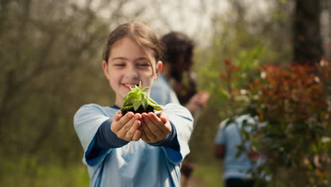 little kid volunteer holding a small seedling with natural soil in hands