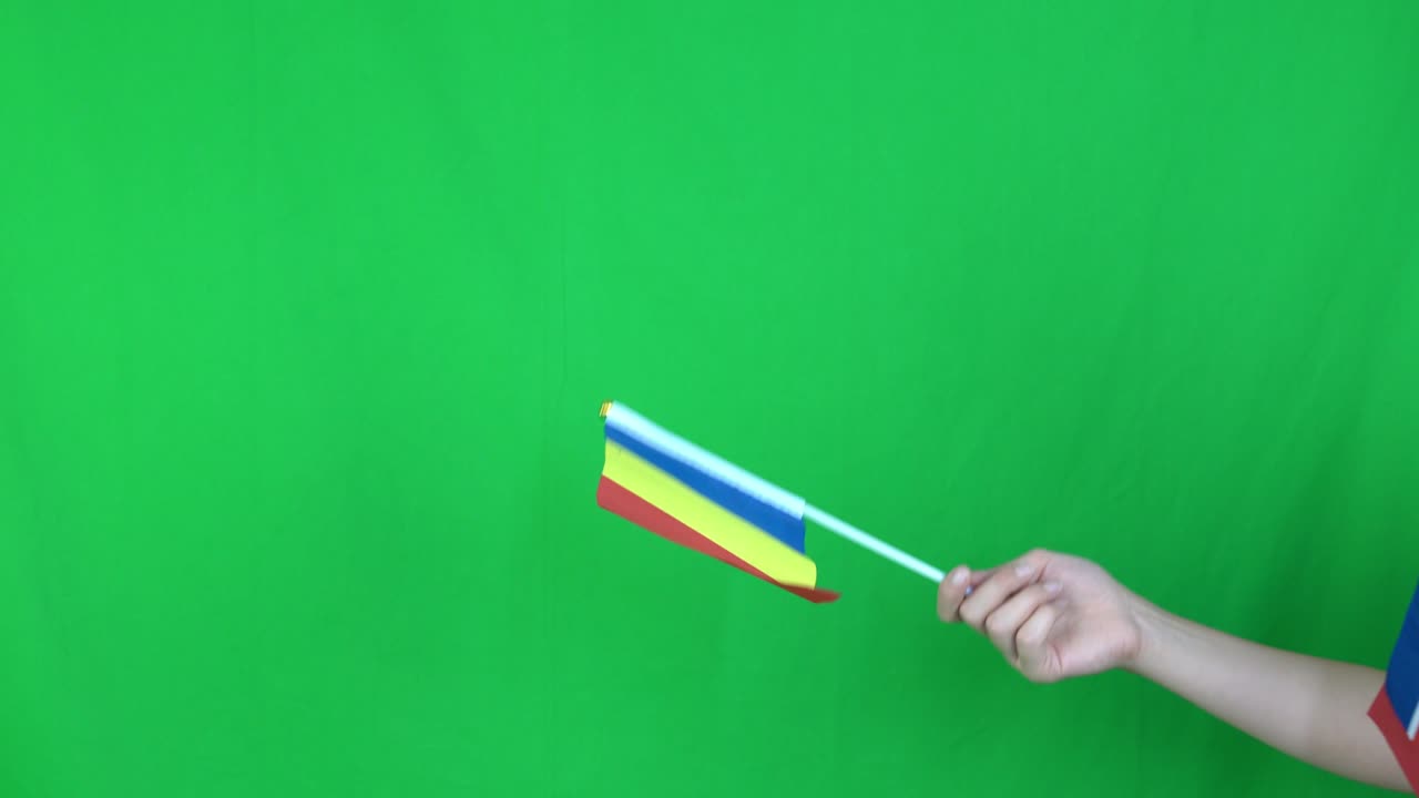 un primer plano de una mano desconocida sosteniendo una bandera rumana en el fondo de la pantalla verde en el estudio.
