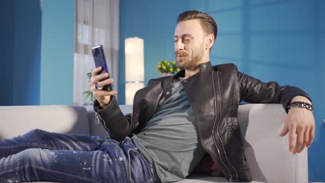 un joven feliz y guapo chateando por video en línea, sonriendo, disfrutando usando su teléfono inteligente en casa.